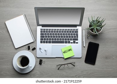 Flat lay composition of note with word Welcome and gadgets on wooden table