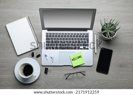 Flat lay composition of note with word Welcome and gadgets on wooden table