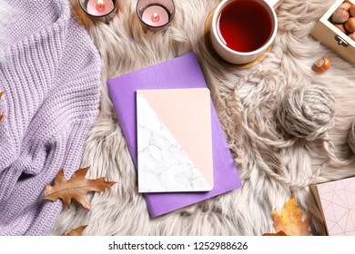 Flat lay composition with notebooks, cup of tea and warm clothes on fuzzy rug