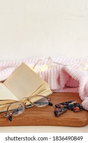 Flat lay composition with open blank paper notebook glasses and natural black chocolate bar with nuts and dried fruits near white knitted blanket and fairy lights.