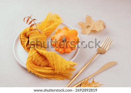 Flat lay composition with orange pumpkin, yellow napkin, dry leaves and golden fork and knife on light background