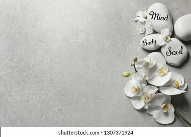 Flat Lay Composition Of Orchid Flowers And Zen Stones With Words Mind, Body, Soul On Light Background. Space For Text 