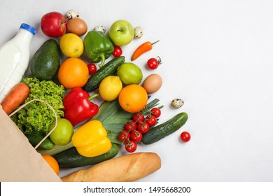Flat lay composition with overturned paper bag and groceries on white table