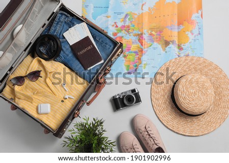 Flat lay composition with packed suitcase and travel accessories on grey background. Summer vacation