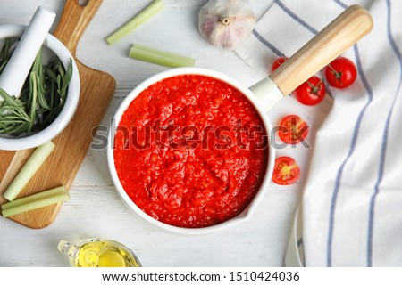 Flat lay composition with pan of tomato sauce on white wooden table