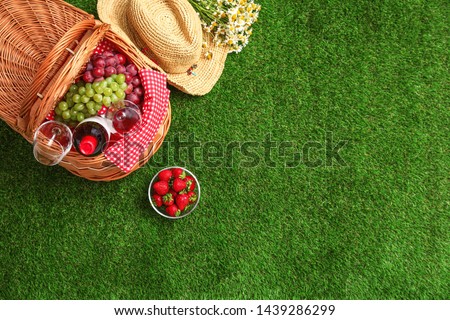 Flat lay composition with picnic basket, wine and fruits on grass, space for text
