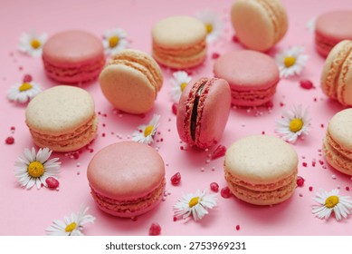 Flat Lay composition of pink and vanilla macarons arranged in pattern with small white daisies and sugar sprinkles on soft pink background. Minimal, elegant dessert concept perfect for bakery, celebration or spring themes. 