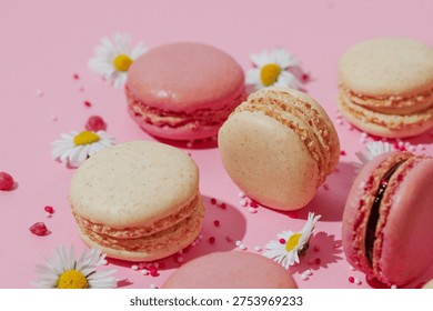 Flat Lay composition of pink and vanilla macarons arranged in pattern with small white daisies and sugar sprinkles on soft pink background. Minimal, elegant dessert concept perfect for bakery, celebration or spring themes. 