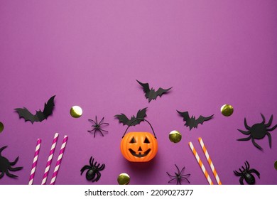 Flat lay composition with plastic pumpkin basket and paper bats on purple background, space for text. Halloween celebration