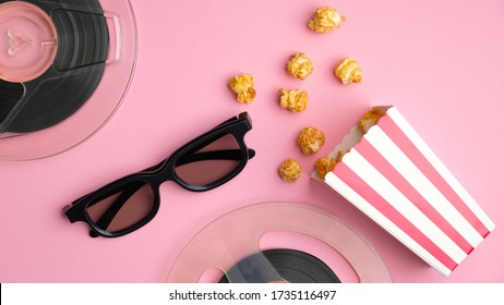 Flat lay composition with popcorn box, 3d glasses and reels of film on pink table top view. Watching movie online with cinema snacks concept.