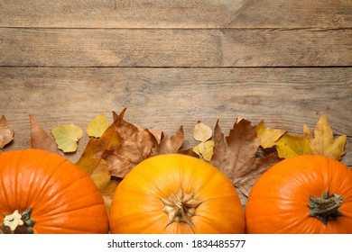 Flat lay composition with pumpkins and autumn leaves on wooden table. Space for text