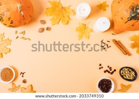 Flat lay composition with pumpkins, autumn leaves and spices on orange background with empty space in middle.