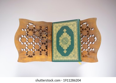 Flat lay composition of rehal with Close Holy Quran on the right rehal with arabic calligraphy meaning of Al Quran on white background