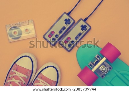 Flat lay composition of retro youth hipster accessories. Gumshoes, cruiser board, joysticks and video cassette on a yellow background. Top view