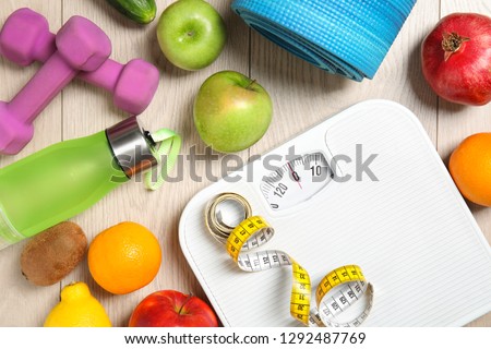 Flat lay composition with scales, healthy food and sport equipment on wooden background. Weight loss