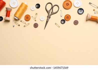 Flat lay composition with scissors and other sewing accessories on light yellow background, space for text