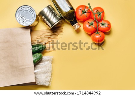 Flat lay composition with a set of products. Paper bag, spaghetti, olive oil, tomatoes, cucumbers, rice and canned food on a yellow background.