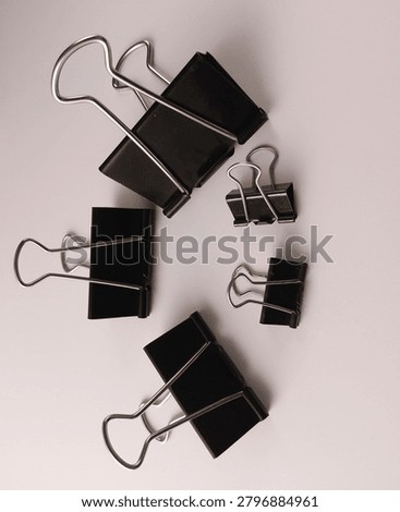 a flat lay composition showing a curved semicircle pattern of black metal binder clips in different sizes on a light surface