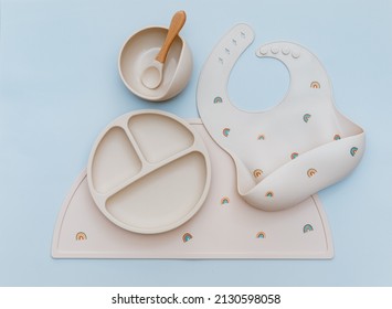 Flat lay composition with silicone baby bib and beige dishware on blue background. Flat lay, top view - Shutterstock ID 2130598058