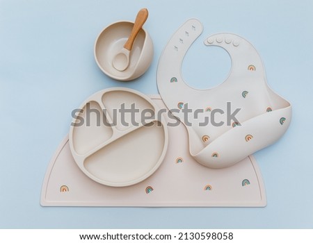 Flat lay composition with silicone baby bib and beige dishware on blue background. Flat lay, top view
