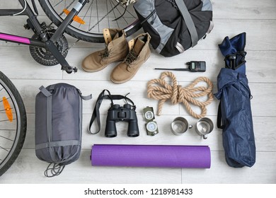 Flat lay composition with sleeping bag, bicycle and camping equipment on wooden background