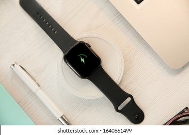 Flat lay composition with smartwatch and wireless charger on white wooden table. Modern workplace accessory
