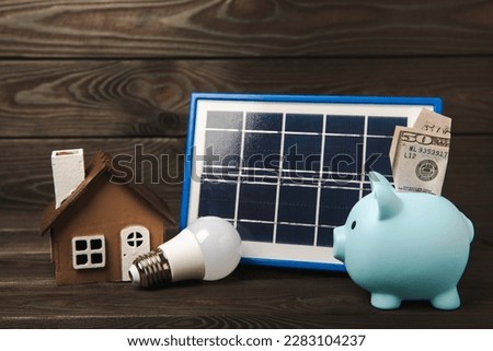 Flat lay composition with solar panel, led lamp, house model, money and piggy bank on brown wood. The concept of saving money and clean energy. Concept of ecology and sustainable development.