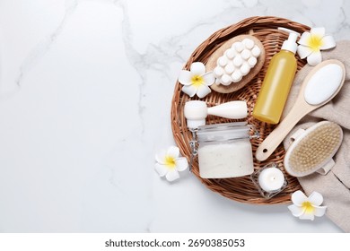 Flat lay composition with spa products and plumeria flowers on white marble table, space for text