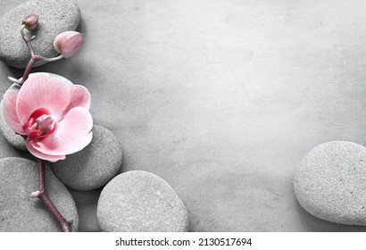 Flat lay composition with spa stones, orchid pink flower on grey background. Spa concept.