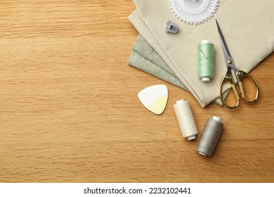 Flat lay composition with spool of threads and sewing tools on wooden table. Space for text