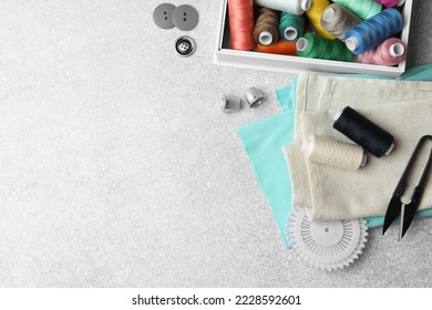 Flat lay composition with spools of threads and sewing tools on light background, space for text
