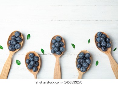 Flat lay composition of spoons with tasty blueberries and leaves on white wooden table, space for text - Powered by Shutterstock