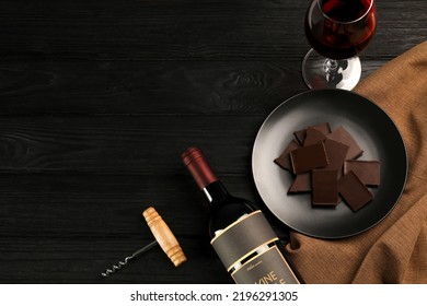 Flat lay composition with tasty red wine and chocolate on black wooden table. Space for text