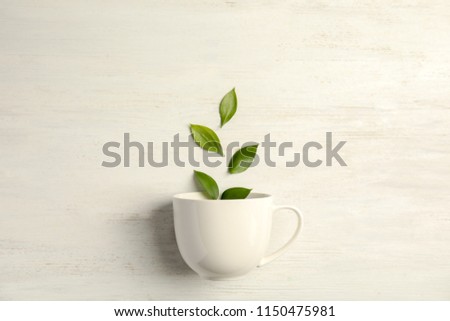 Flat lay composition with teacup and green leaves on wooden background
