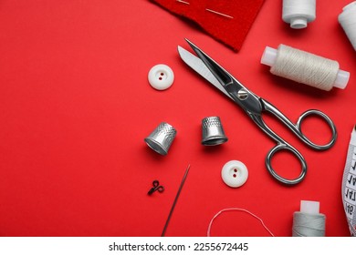 Flat lay composition with thimbles and different sewing tools on red background. Space for text
