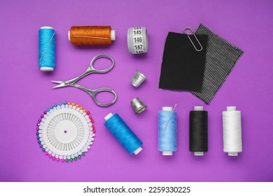Flat lay composition with thimbles and different sewing tools on purple background