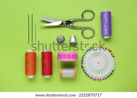 Flat lay composition with thimbles and different sewing tools on green background