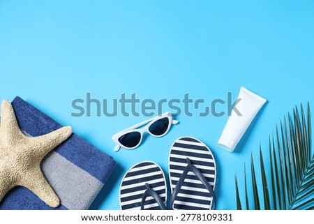 Flat lay composition with towel and other beach accessories on light blue background. Space for text