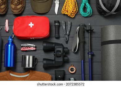 Flat lay composition with trekking poles and other hiking equipment on dark grey wooden background