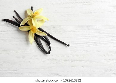 Flat lay composition with vanilla sticks and flowers on wooden background. Space for text
