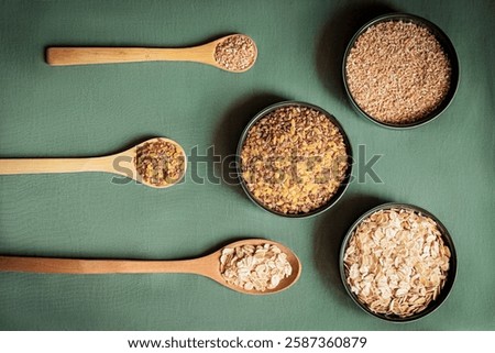 Flat lay composition of various grains and cereals in wooden spoons and bowls on a green background. Healthy eating, organic food, and nutrition concept. Minimalist food styling