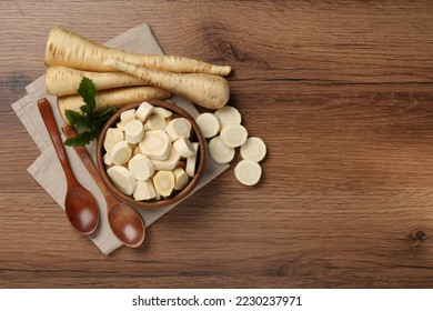 Flat lay composition with whole and cut fresh ripe parsnips on wooden table. Space for text