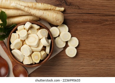 Flat lay composition with whole and cut fresh ripe parsnips on wooden table. Space for text