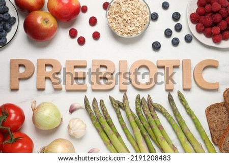 Flat lay composition with word Prebiotic made of wooden letters and different products on white marble table
