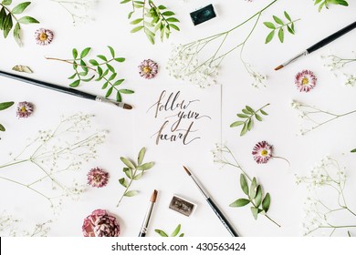Flat lay composition, workspace with quote follow your heart written in calligraphy style on white paper. Artist working place