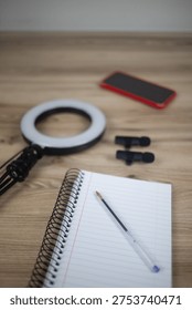 Flat Lay of Content Creator Essentials - Ring Light, Wireless Lavalier Microphones, Smartphone, and Spiral Notebook with Pen on Wooden Desk
