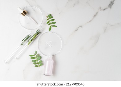 Flat lay of cosmetics serum and and laboratory glassware with fresh leaves on marble background. Organic cosmetics. Top view flat lay, copy space. Cosmetics, SPA branding, mock-up