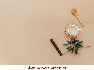 Flachlage mit handwerklichem Notizbuch, Tasse Kaffee und trockene Blumen auf braunem Hintergrund. Neutral flacher Lauf, Draufsicht. Minimaler trendiger Hintergrund für Blogger