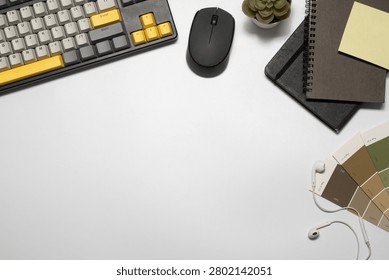 Flat lay of a creative designer's workspace featuring a yellow mechanical keyboard, wireless mouse, spiral notebooks, color palette swatches, earphones, and succulent plant.