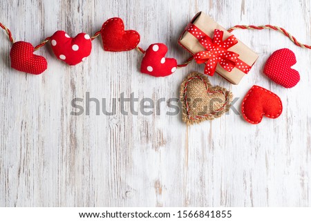 Flat lay cute composition with handmade fabric red hearts. Gift box with ribbon bow on wooden table. Happy birthday or anniversary congratulation. Romantic message template with copy space.